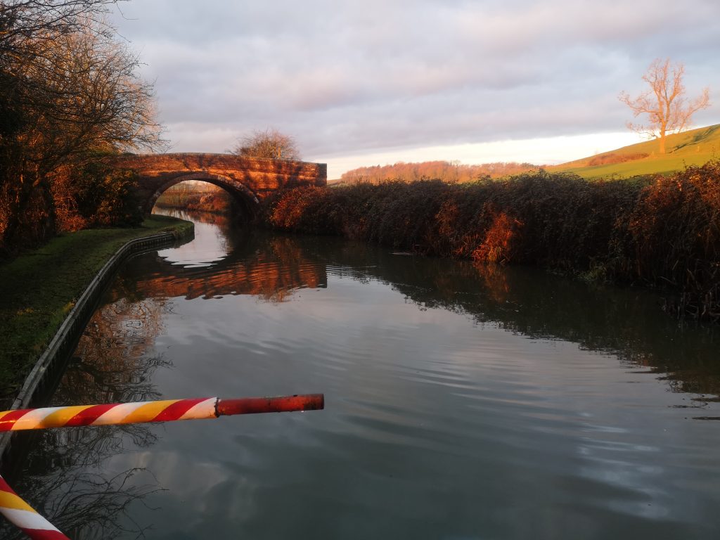 a boat tiller in front of the canal and behind can be seen a canal bridge.  to the right a hill rises 
